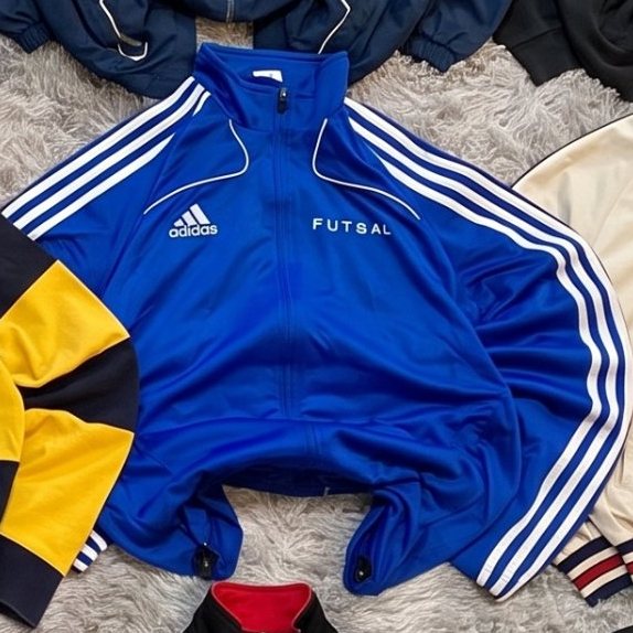 Chaqueta de chándal Adidas Futsal azul extendida sobre una alfombra gris
