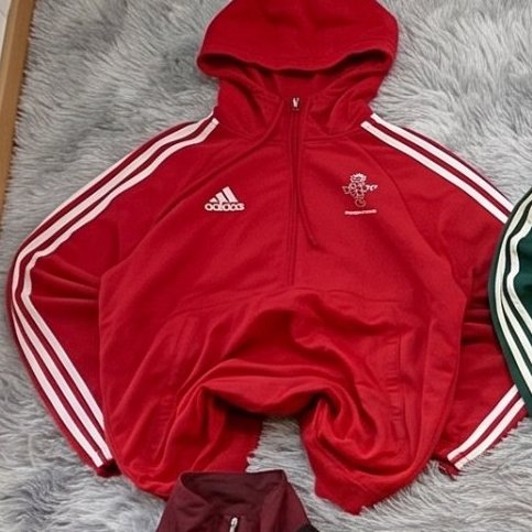 Sudadera de media cremallera Adidas roja con capucha extendida sobre una alfombra gris