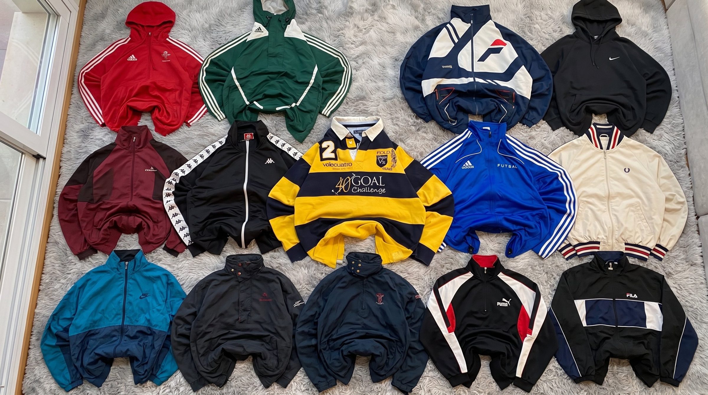 Catorce chaquetas y sudaderas de chándal vintage ordenadas sobre una alfombra gris