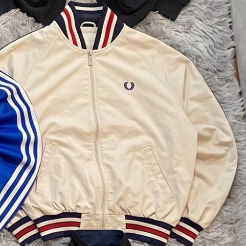 Chaqueta con cremallera Fred Perry crema extendida sobre una alfombra gris
