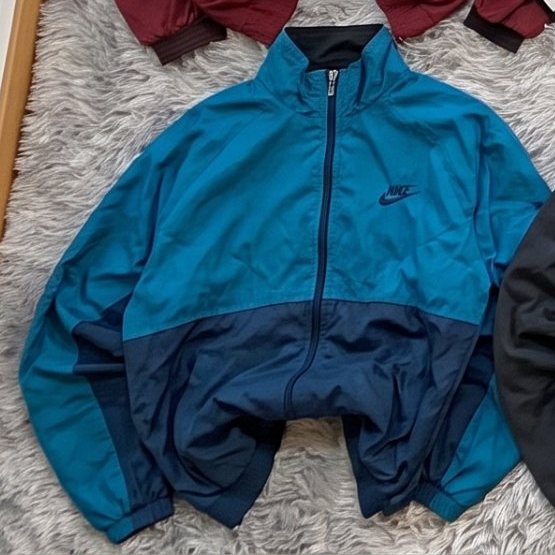 Cortavientos Nike turquesa y marino extendida sobre una alfombra gris