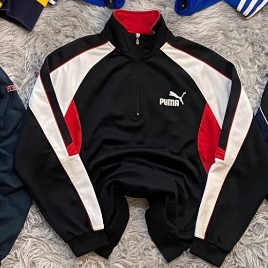 Chaqueta de media cremallera Puma negra y roja extendida sobre una alfombra gris