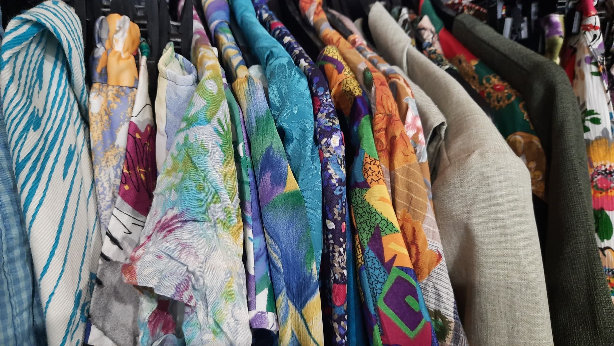 Perchero lleno de camisas vintage estampadas en una tienda de segunda mano